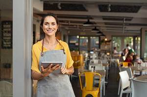 small business owners standing outside cafe with tablet smiling at camera